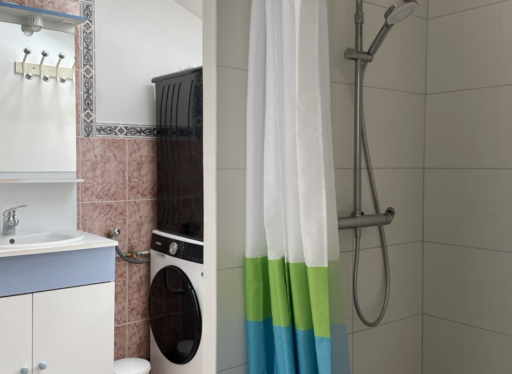 Salle d’eau fonctionnelle avec douche, machine à laver, sèche-linge et lavabo